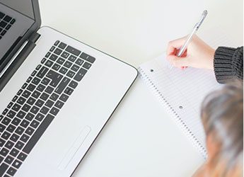 Minimalistic workspace with laptop and female hands writing in notebook