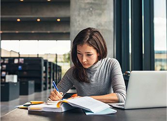 Female student taking notes from a book at library